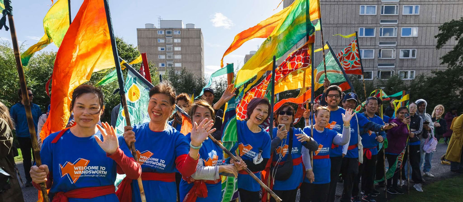 Local residents are pictured waving and carrying silk flags as part of the Urban Flow event. Alton Estate buildings can be seen in the background.