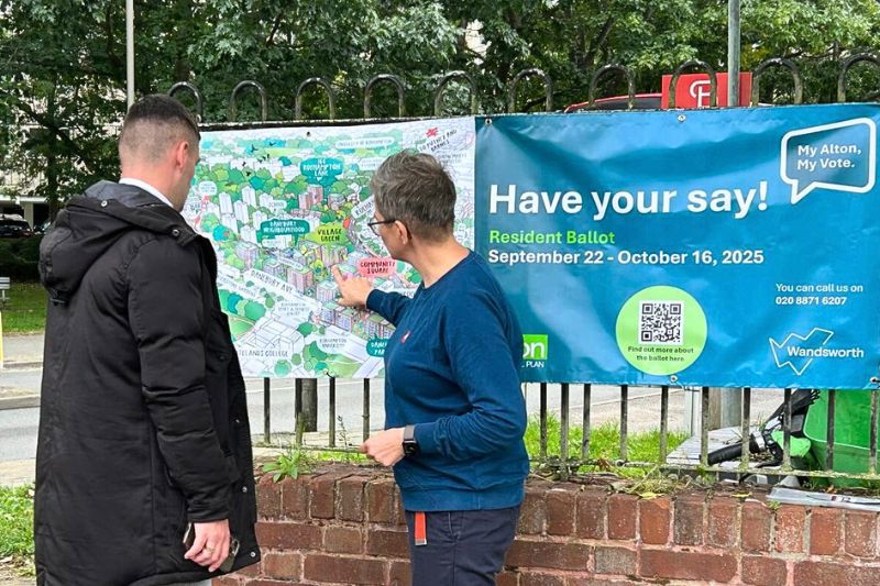 Two people are pictured looking at a banner featuring an illustrative aerial view of the Alton