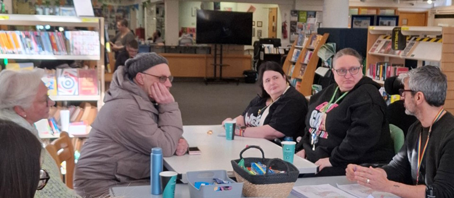 An image showing people sitting around a table in a library, having a discussion.