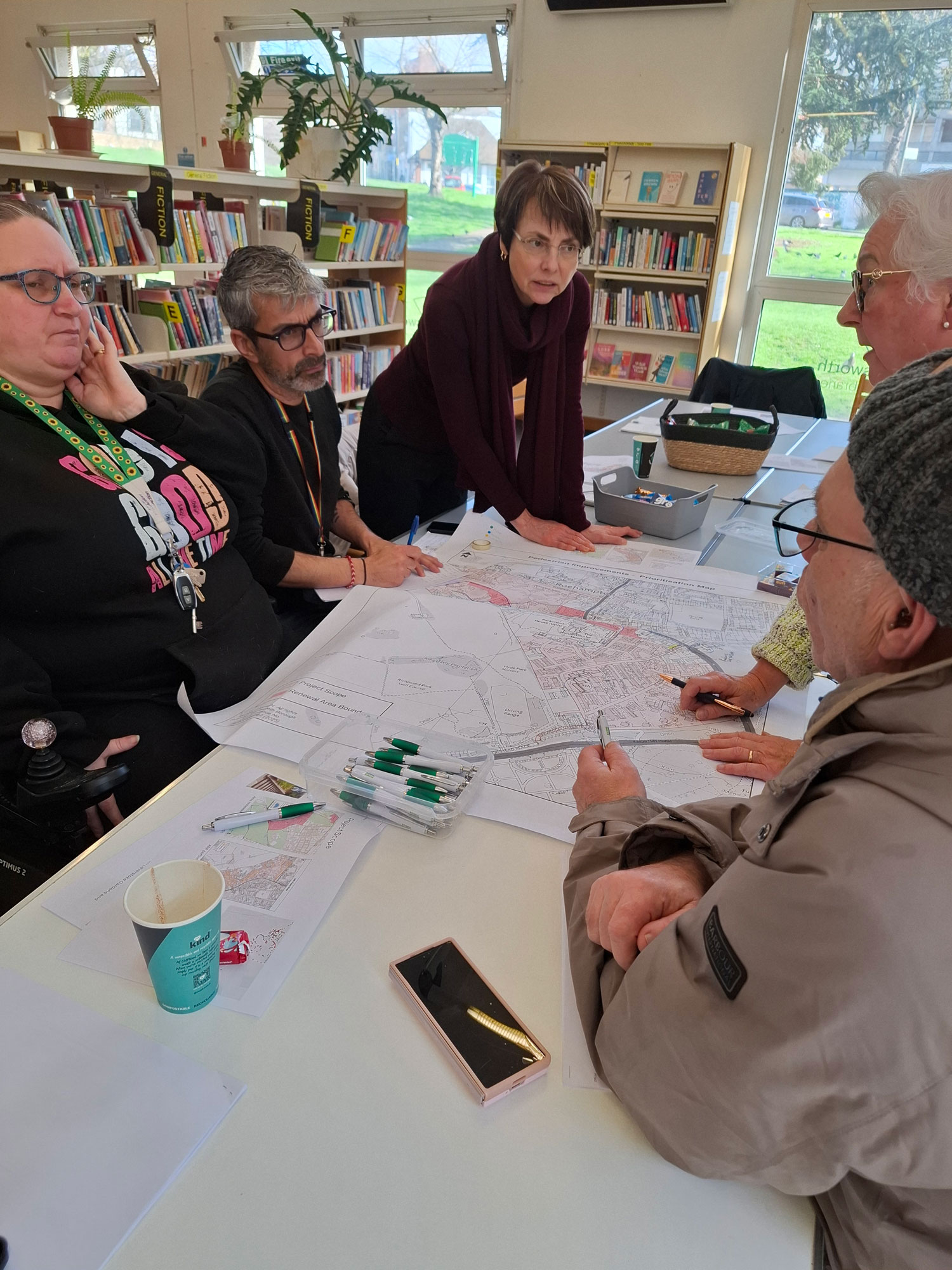 People are pictured sitting and standing around a table, having a discussion and studying a plan.