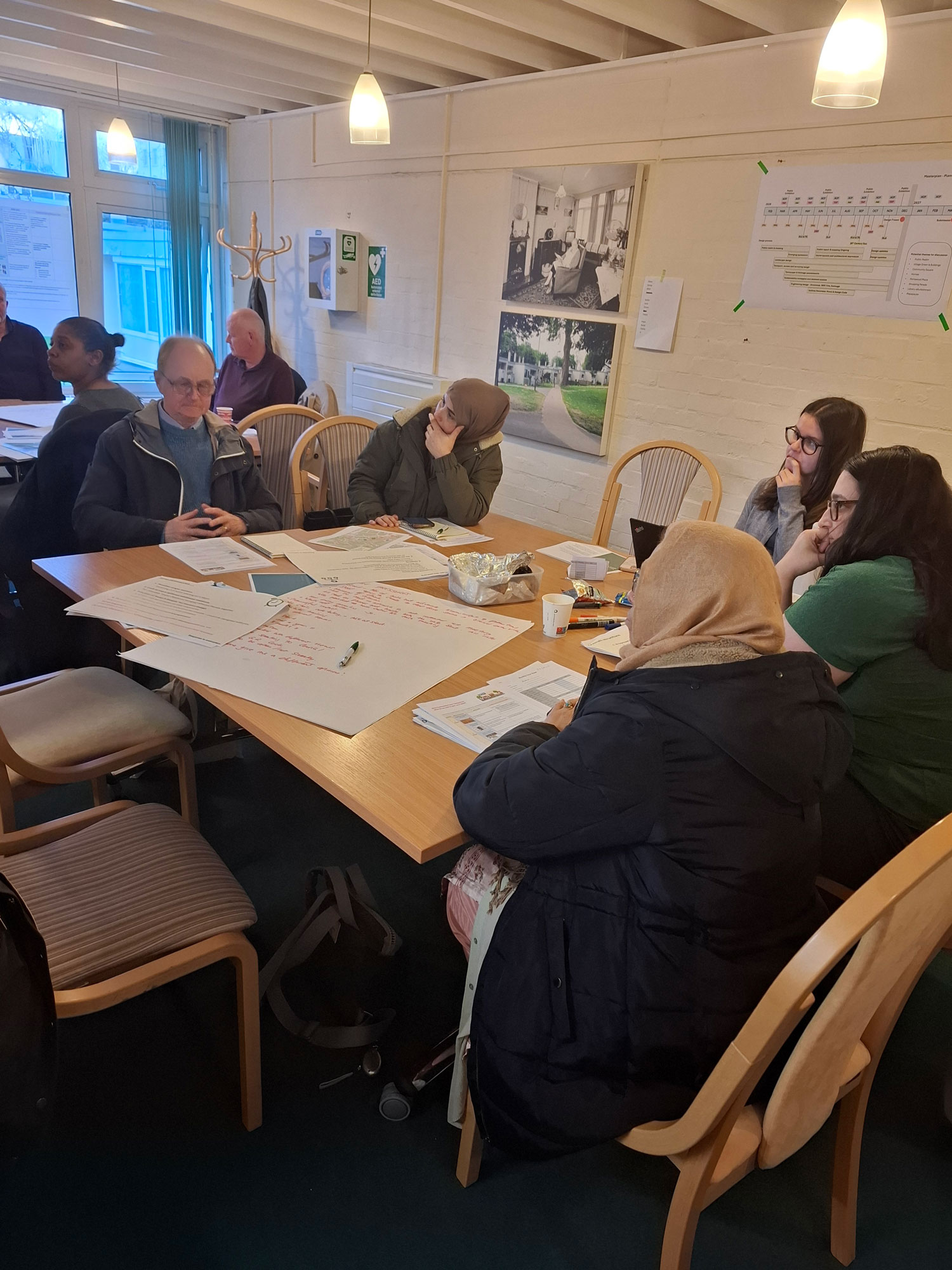 Groups of people are pictured sitting around tables reviewing papers, making notes and listening to speakers