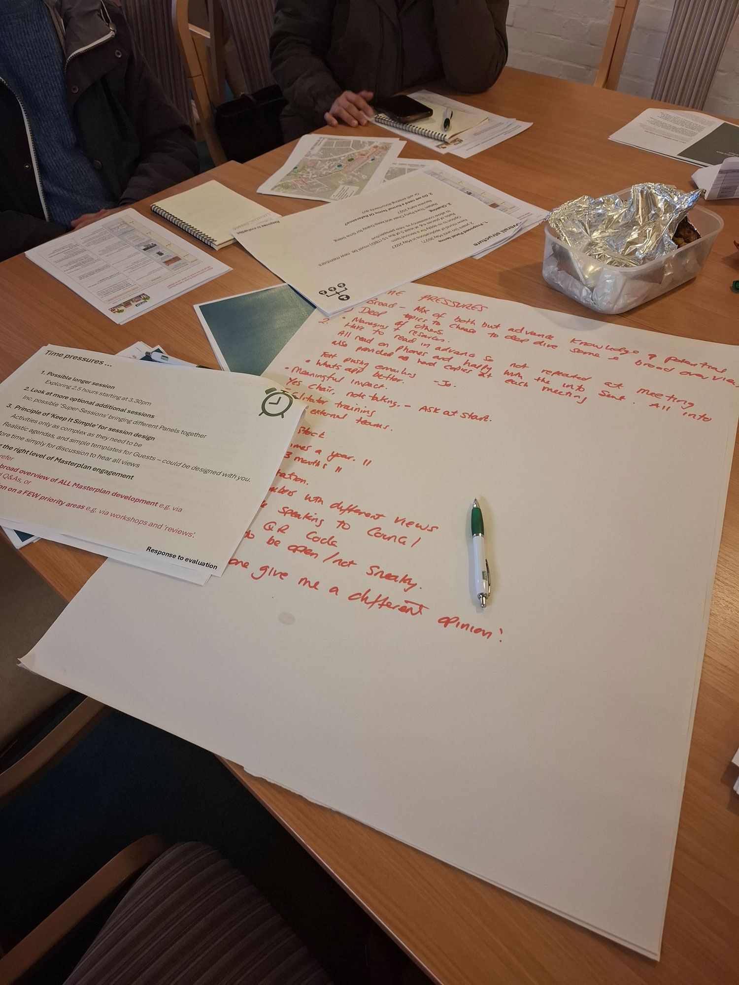 An image shows handwritten notes and printed notes on various sheets of paper. From the edges of the image, it is clear that there are people sitting around a table.