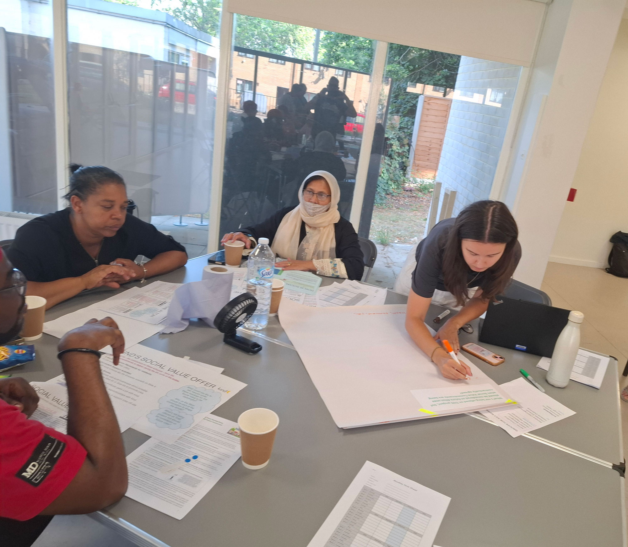 Four people are pictured sitting around a table, having a discussion. One of the people is writing notes on a large sheet of paper.