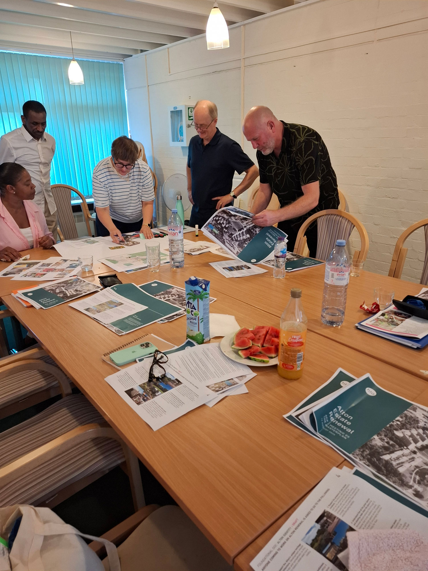 Members of the Alton Community Panel are pictured sitting and standing around a table, reviewing pictures and plans