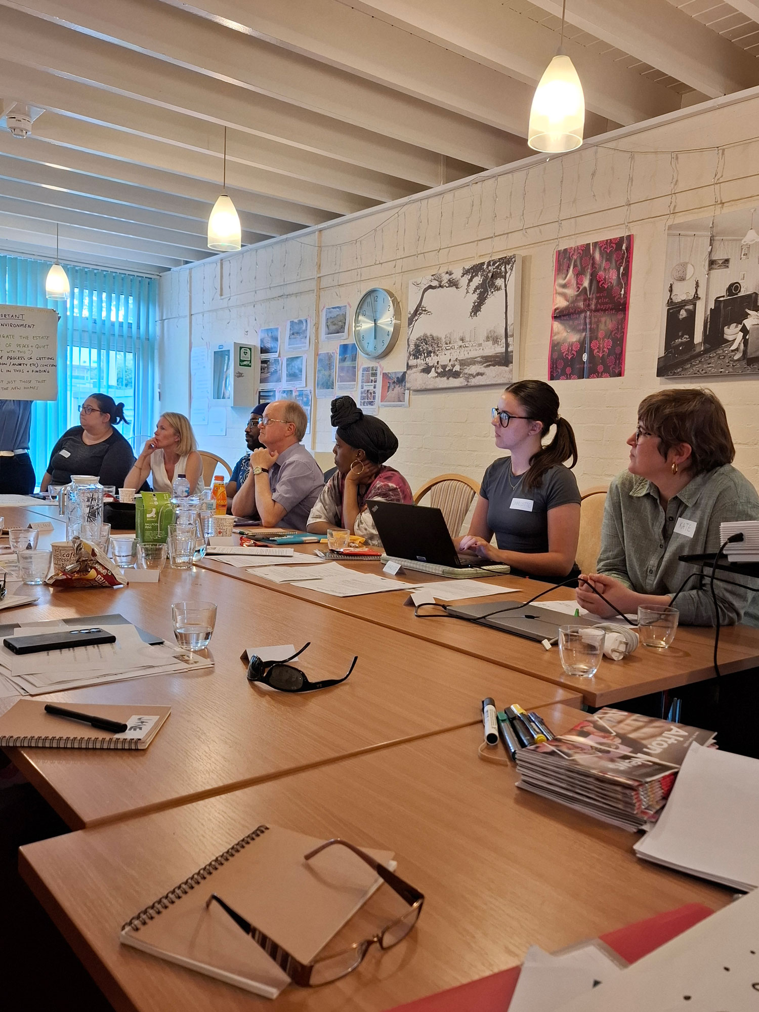 People are pictured sitting around a table, looking towards the end of the table where someone is holding up a flipchart with writing on it.