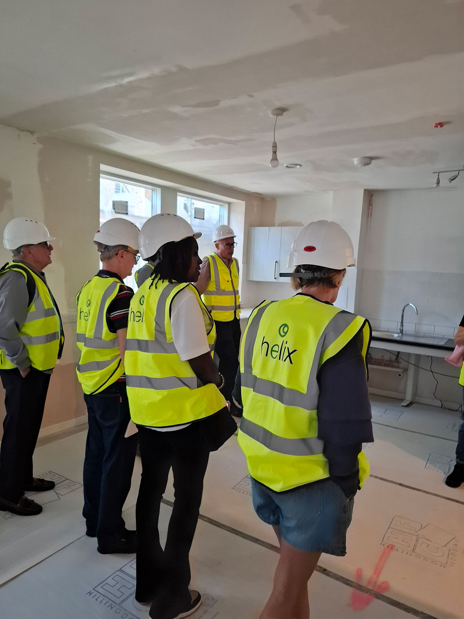 A group of people wearing hard hats and high visibility vests is pictured inside a new building that is being fitted out.