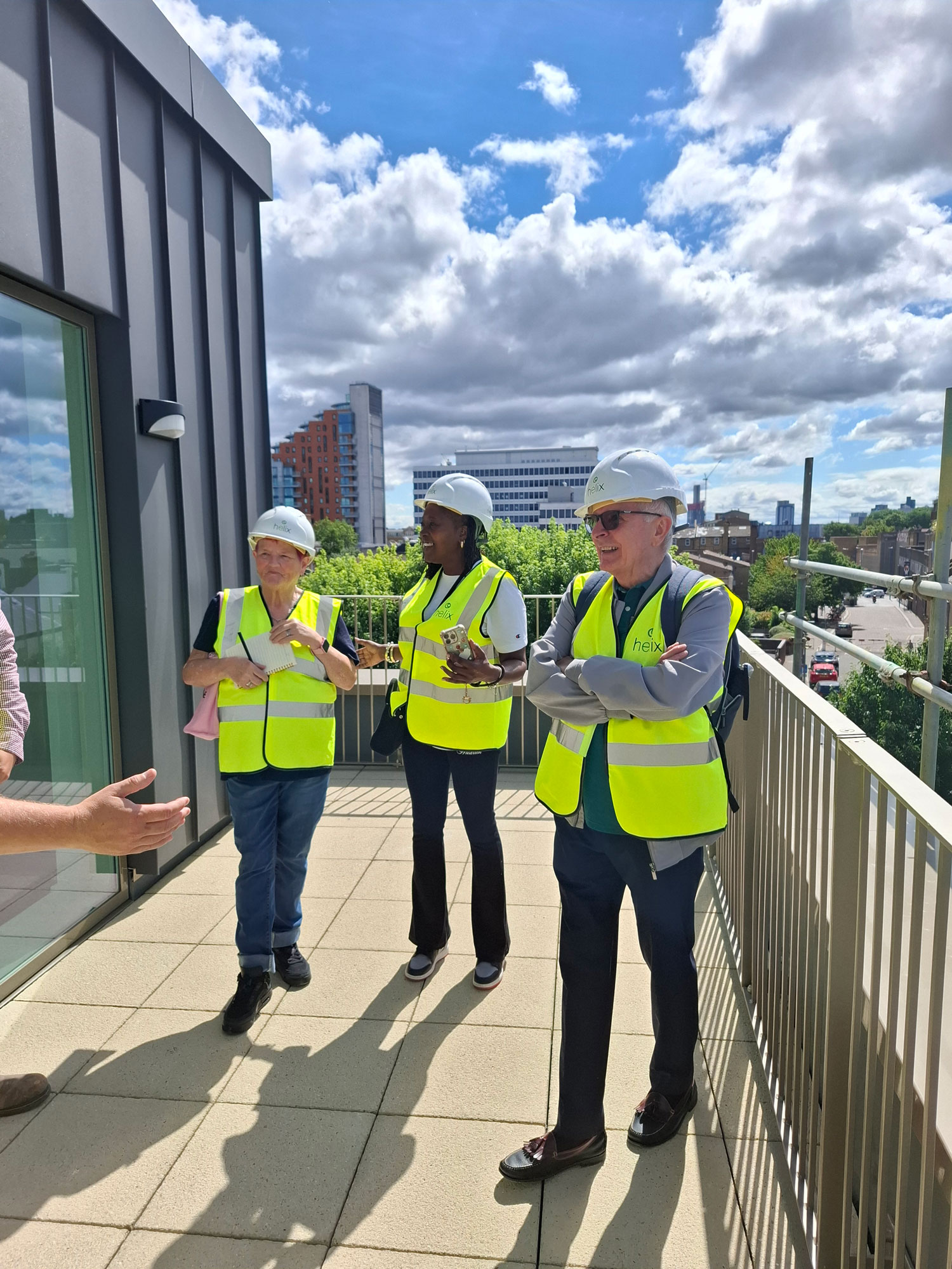 A group of people wearing hard hats and high visibility vests is pictured on the balcony of a new building.