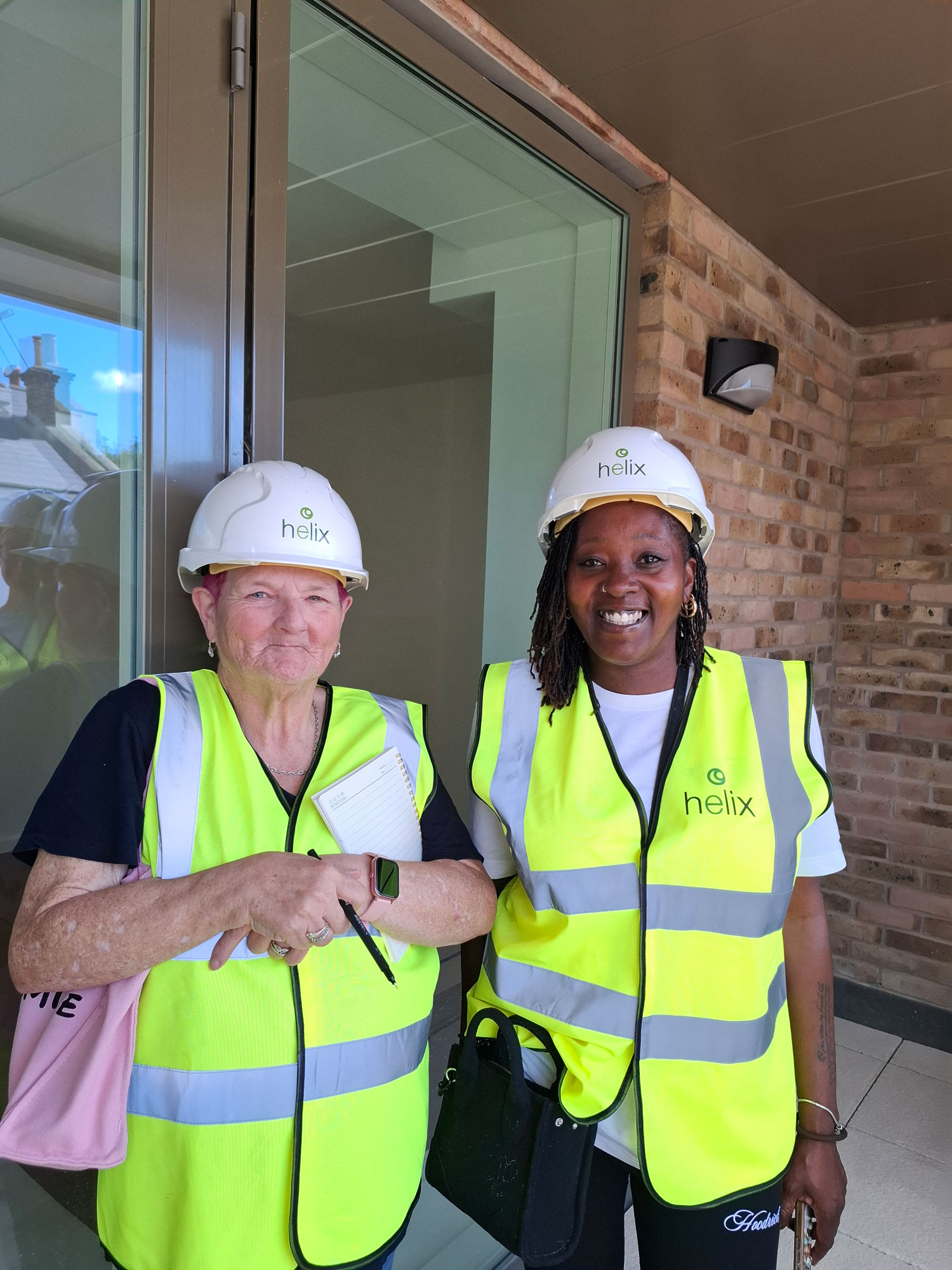 Two people wearing hard hats and high visibility vests are pictured visiting a new development.