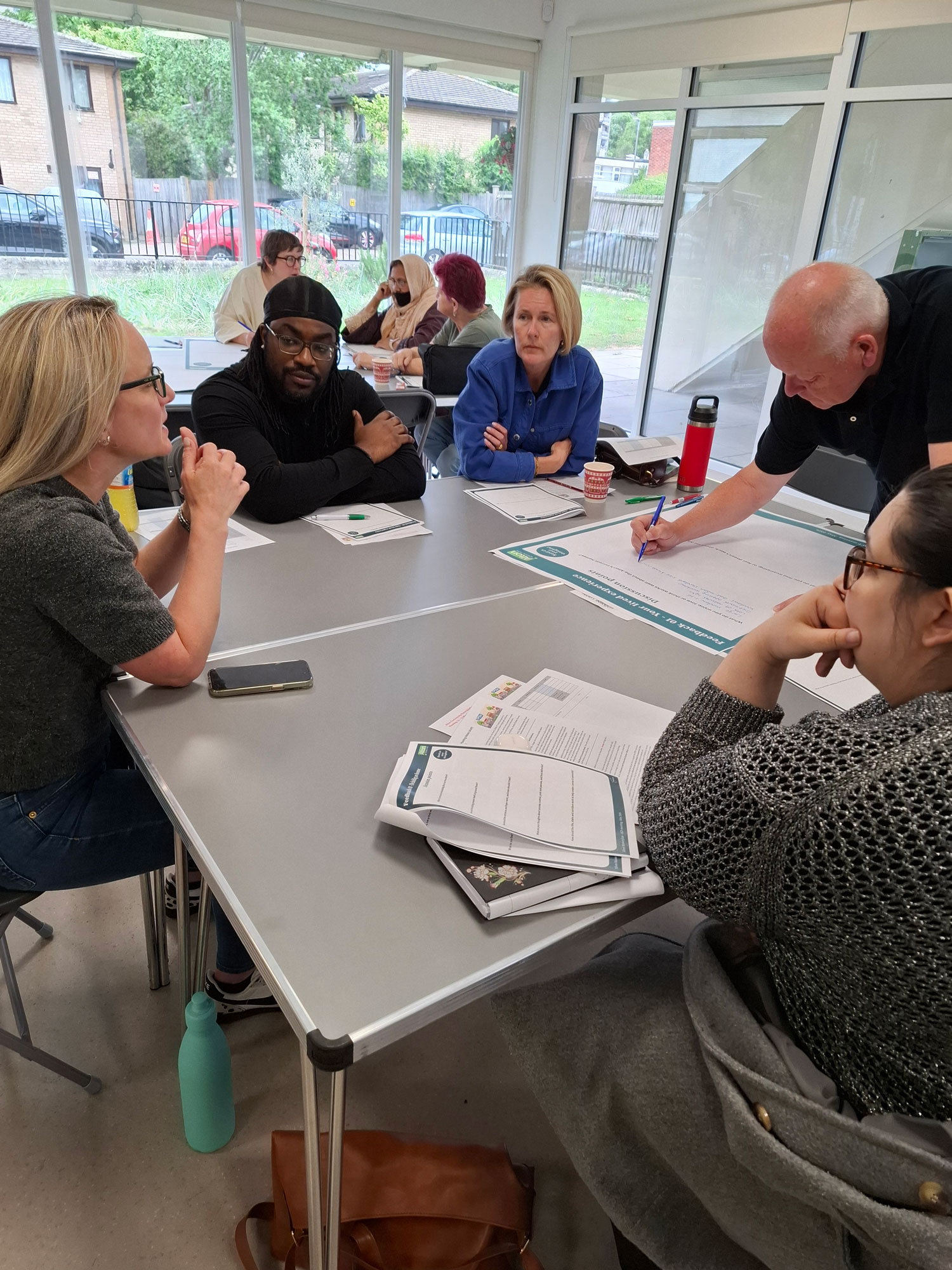 People are pictured sitting around tables. One person is writing notes on a large sheet of paper.