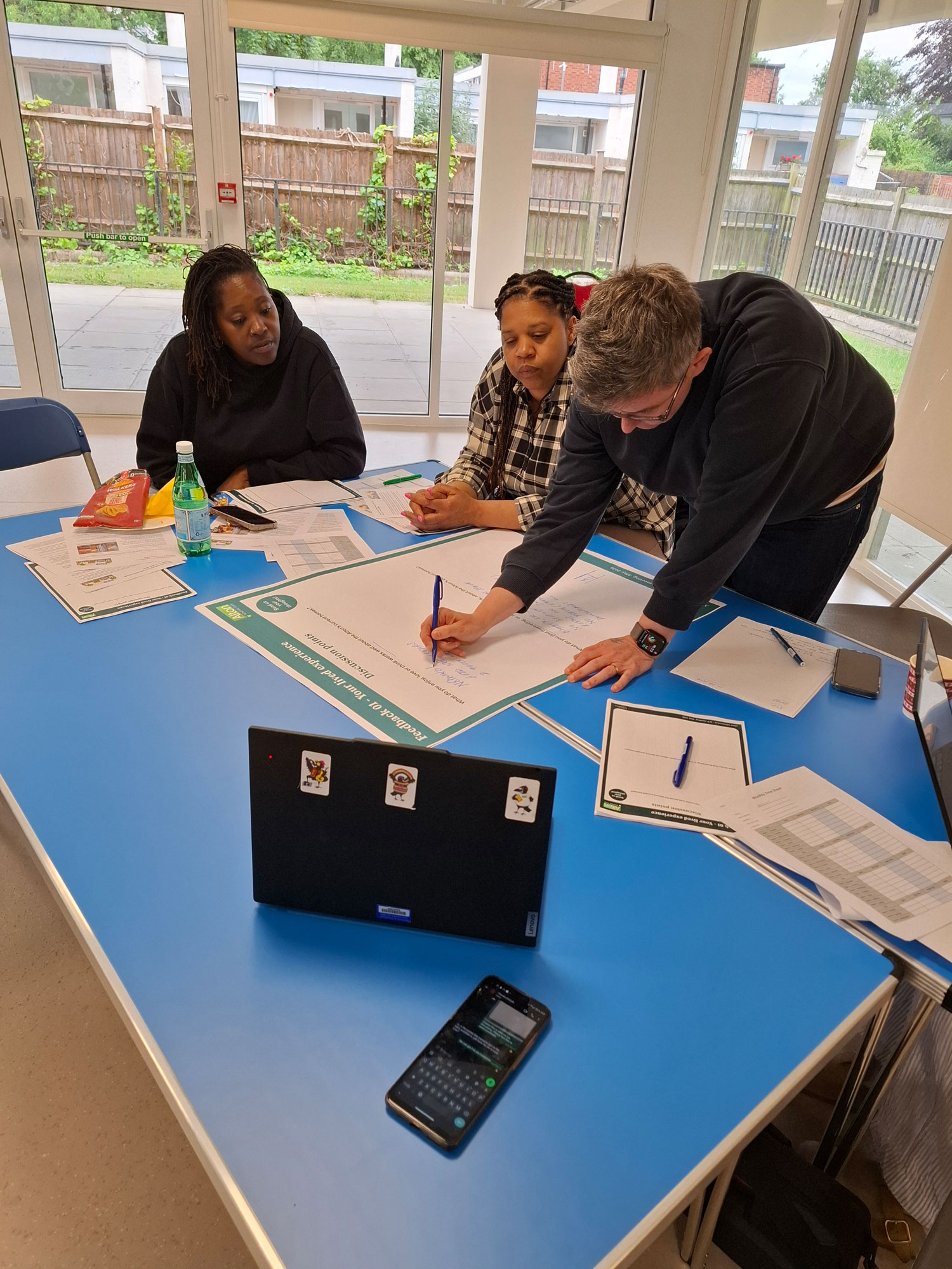 People are pictured sitting around a table. One person is writing notes on a page, with documents spread out across the table.