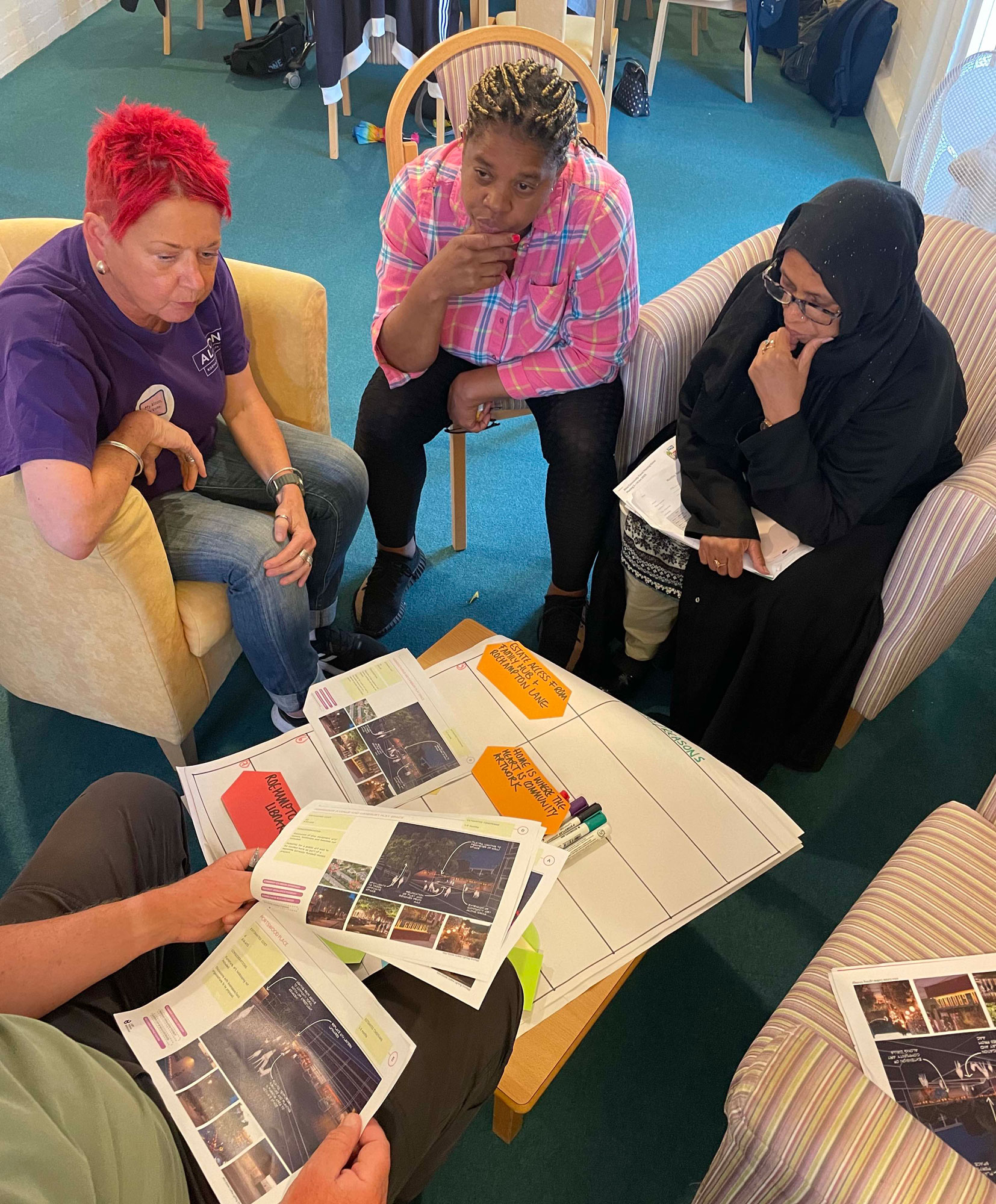A group of people are sitting around a coffee table, looking and notes and images and having a discussion.