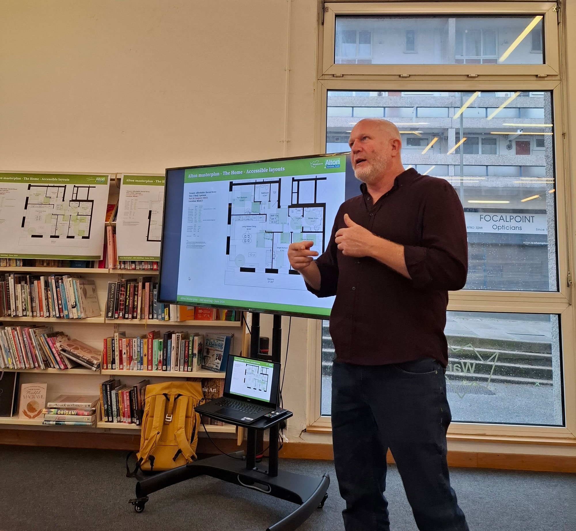 A presenter is pictured, standing in front of a presentation screen, talking about accessible home layouts.
